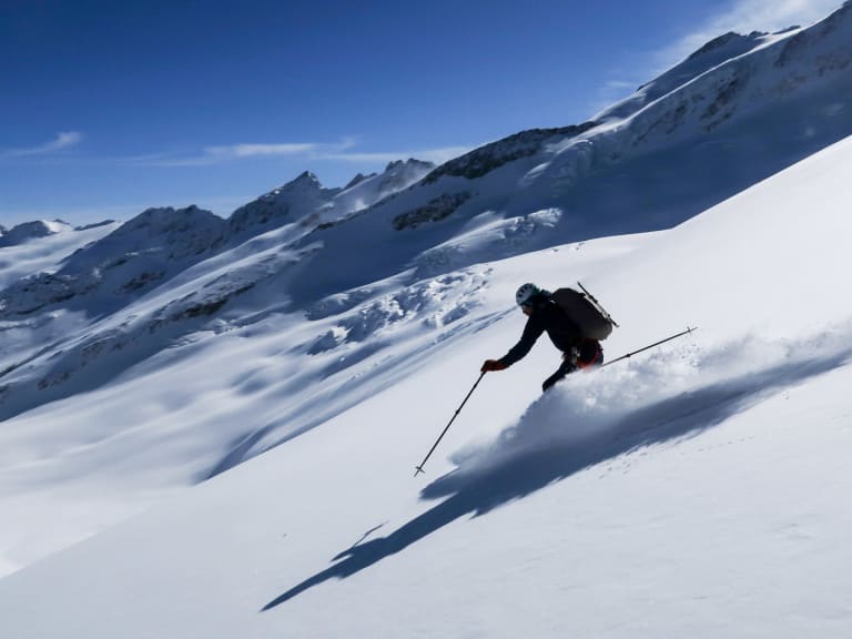 Bergführer Sebastian Vendt fährt einen steilen Hang mit Skiern hinab und wirbelt Neuschnee auf.