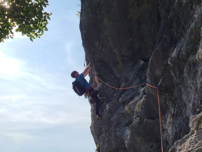 An grauer Kalksteinwand klettert Bergführer Lukas Degen mit blauem Oberteil und orangefarbenem Seil.