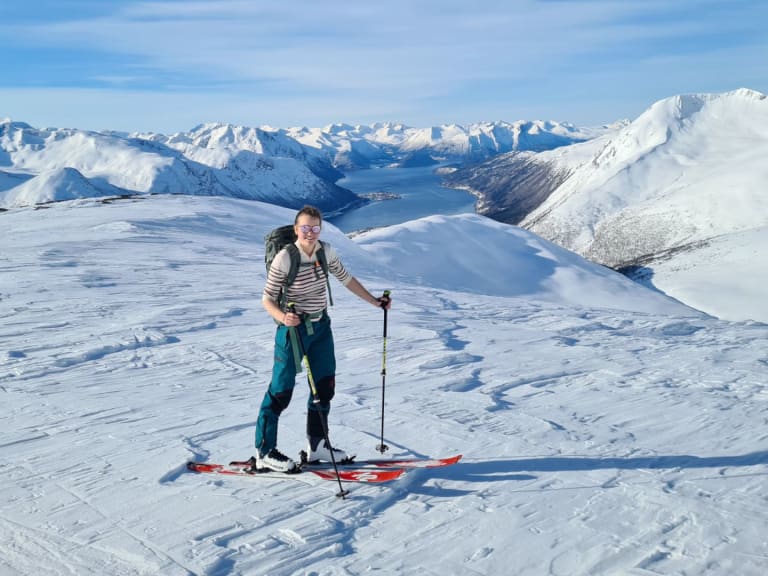 Bergwanderführerin Magdalena Strötz steht auf roten Tourenski in einer Schneelandschaft mit Fjord und Bergen im Hintergrund.