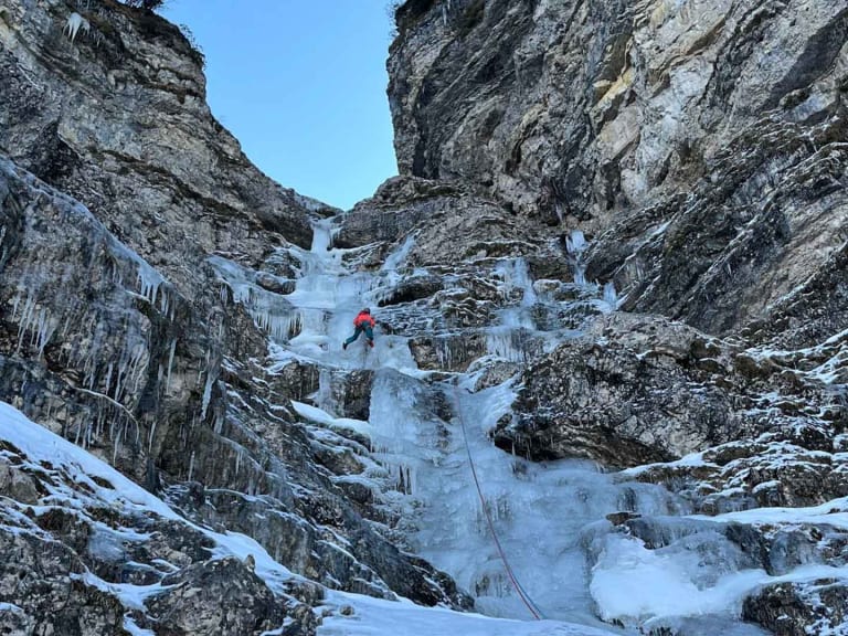 Bergführerin Monika Hümmer in roter Kleidung klettert an gefrorenem Wasserfall mit Eiszapfen.