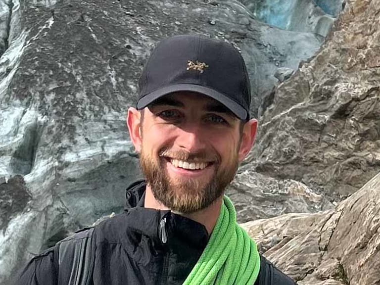 An einer hellen Felswand posiert Bergführer Joshua Wontroba mit grünem Kletterseil über der Schulter.