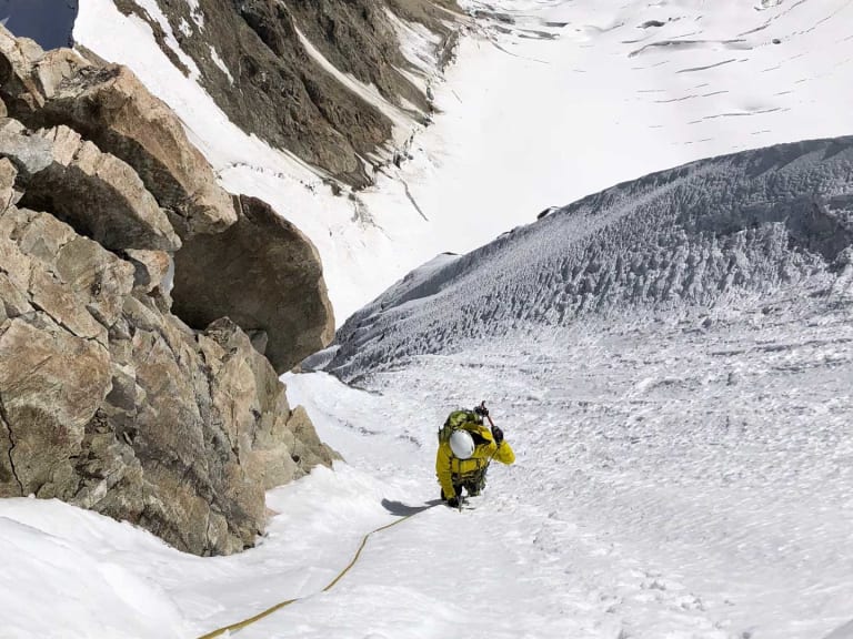 In gelber Winterbekleidung steigt Bergführer Simon Taffner einen steilen, verschneiten Hang hinauf, gesichert am Seil.