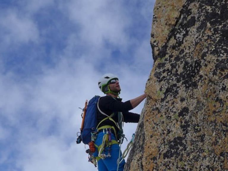 Bergführer Simon Taffner klettert in blauer Kleidung mit grünem Helm an einer steilen Felswand aus gelblich-grauem Gestein.