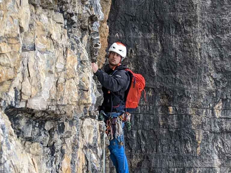 An grauer Kalksteinwand klettert Bergführer Christoph Meysel mit weißem Helm und Kletterausrüstung.