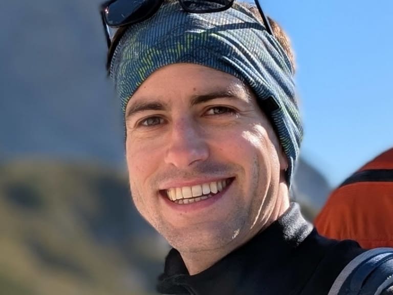 Lächelnder Bergführer Christoph Meysel mit gestreifter Mütze und orangem Rucksack vor Felswänden.