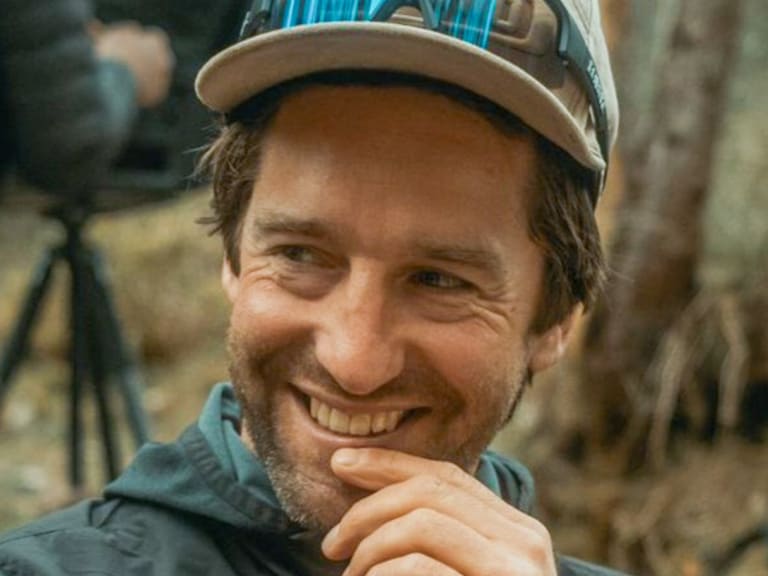 Bergführer Christian Brüderl lächelt freundlich in die Kamera und trägt eine türkise Softshell-Jacke mit Baseballkappe.