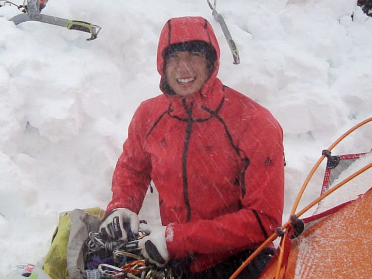 Bei einer Expedition sitzt Bergführer Korbinian Schmidtner in roter Daunenjacke vor dem orangem Zelt im Schnee.