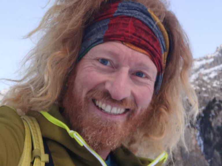 Bergführer Roland Wimmer macht ein Selfie vor schneebedeckten Felswänden in winterlicher Gebirgslandschaft.