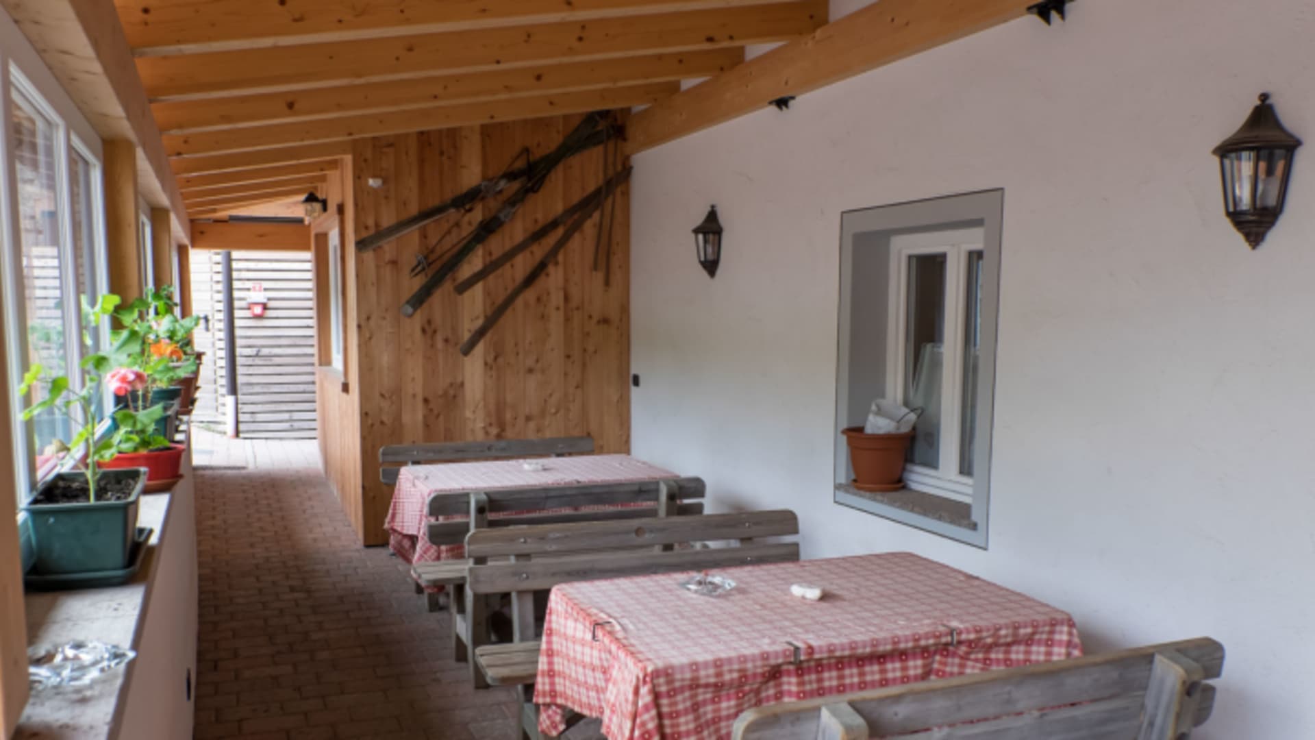 Überdachte Terrasse des Rifugio Carlo Valentini mit Holztischen und traditionellen rot-weiß karierten Tischdecken.