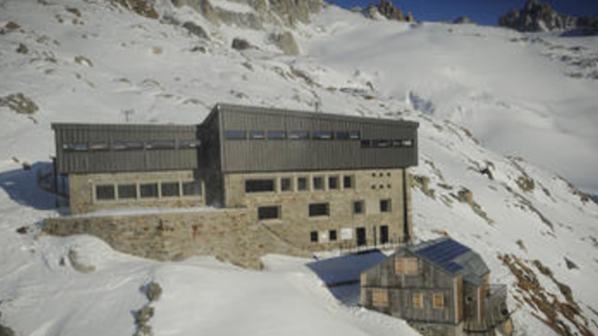 Luftaufnahme des Refuge Albert 1er umgeben von verschneiten Berghängen und Felswänden im Hochgebirge.