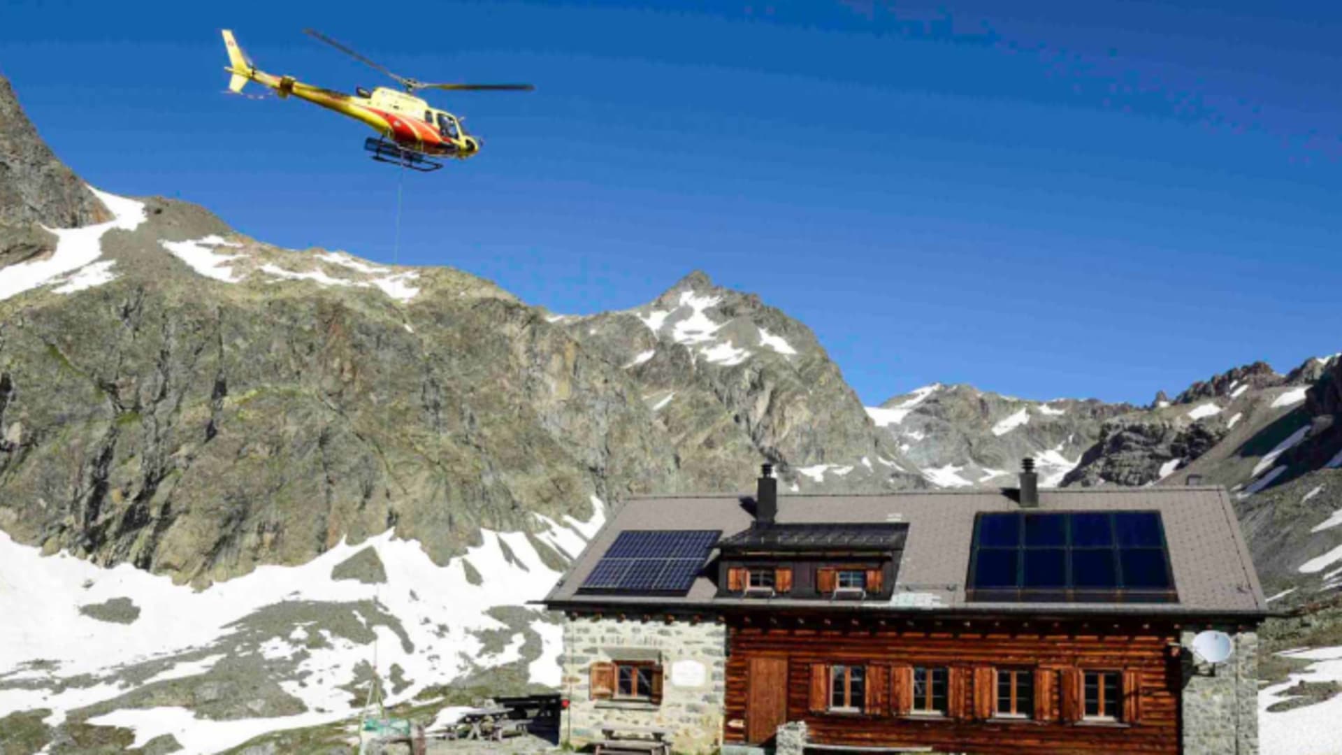 Hubschrauber transportiert Material zur Chamanna Jenatsch inmitten der hochalpinen Landschaft der Bergkette.