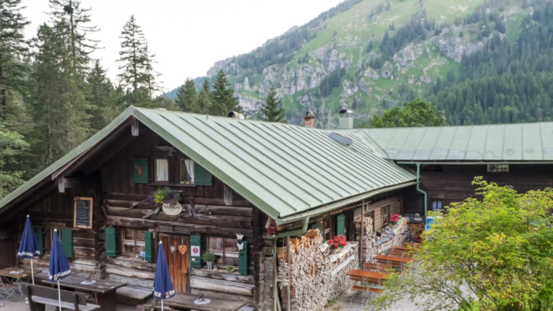 Gesamtansicht der Kenzenhütte mit Holzanbau vor steilen bewaldeten Berghängen im Sommer.