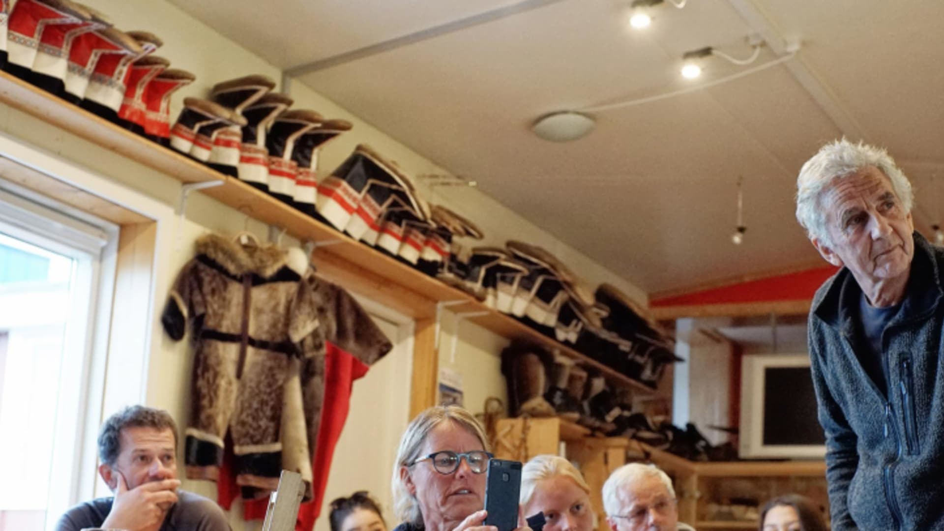 Gäste sitzen im Gemeinschaftsraum des The Red House, Tasiilaq (Ostgrönland) an Holztischen.