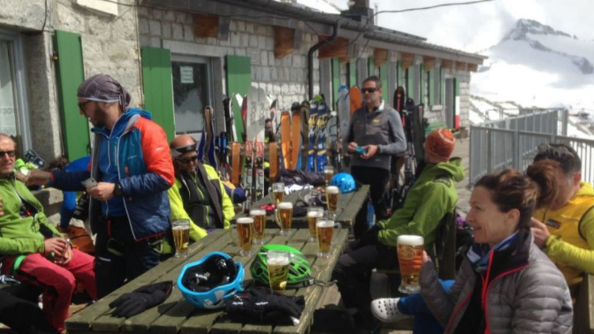 Skitourengeher pausieren mit Bier vor dem Rifugio Gen. Achille Papa, ihre Skier lehnen an der Hüttenwand.