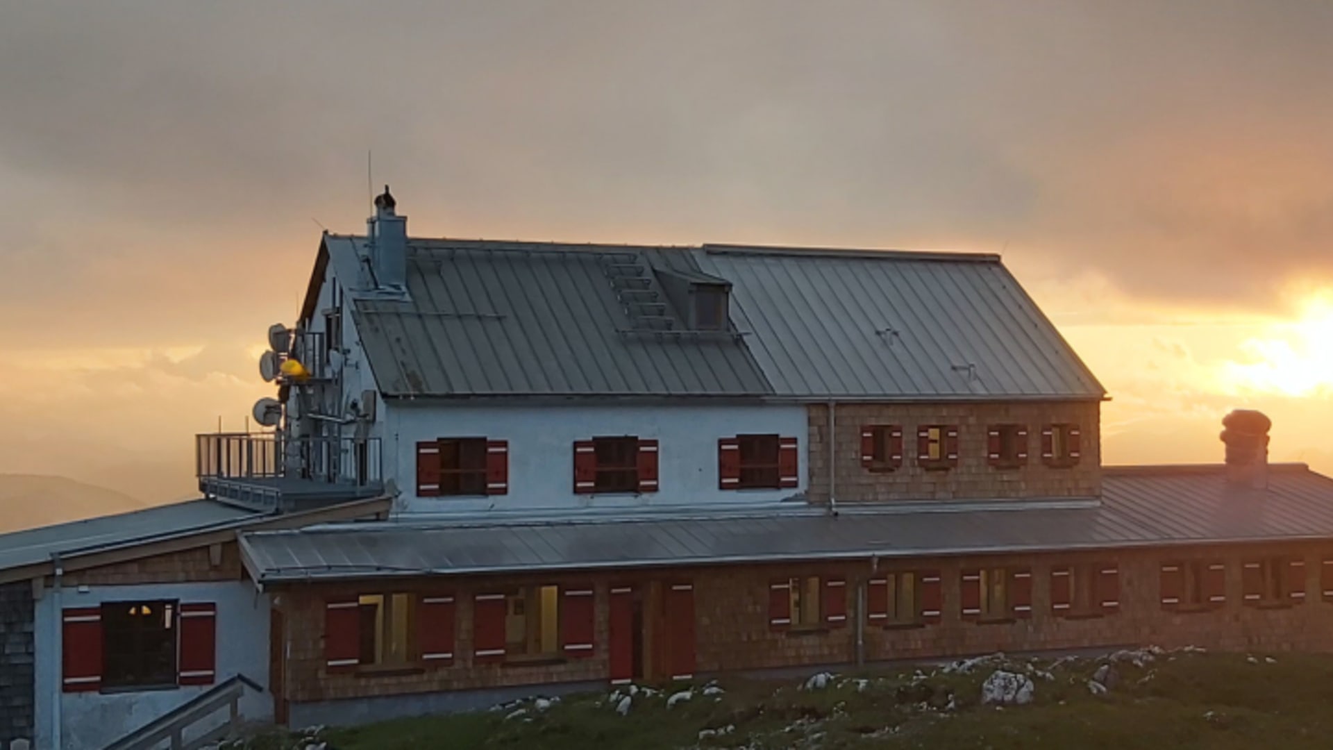 Das Stöhrhaus in warmer Abendbeleuchtung mit alpiner Architektur und roten Fensterläden bei Sonnenuntergang.