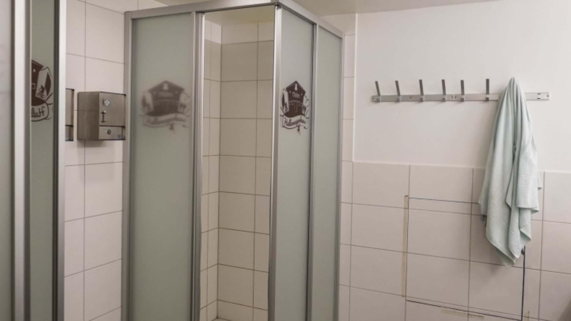 Moderne Eckdusche im Hallerangerhaus mit Glastüren, weißen Fliesen und Seifenspender an der Wand.