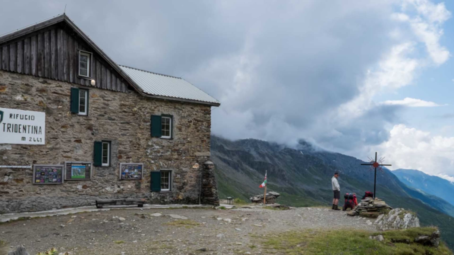 Außenansicht der Birnlückenhütte auf 2441 m mit Steinmauern und Gipfelkreuz vor der Hütte.