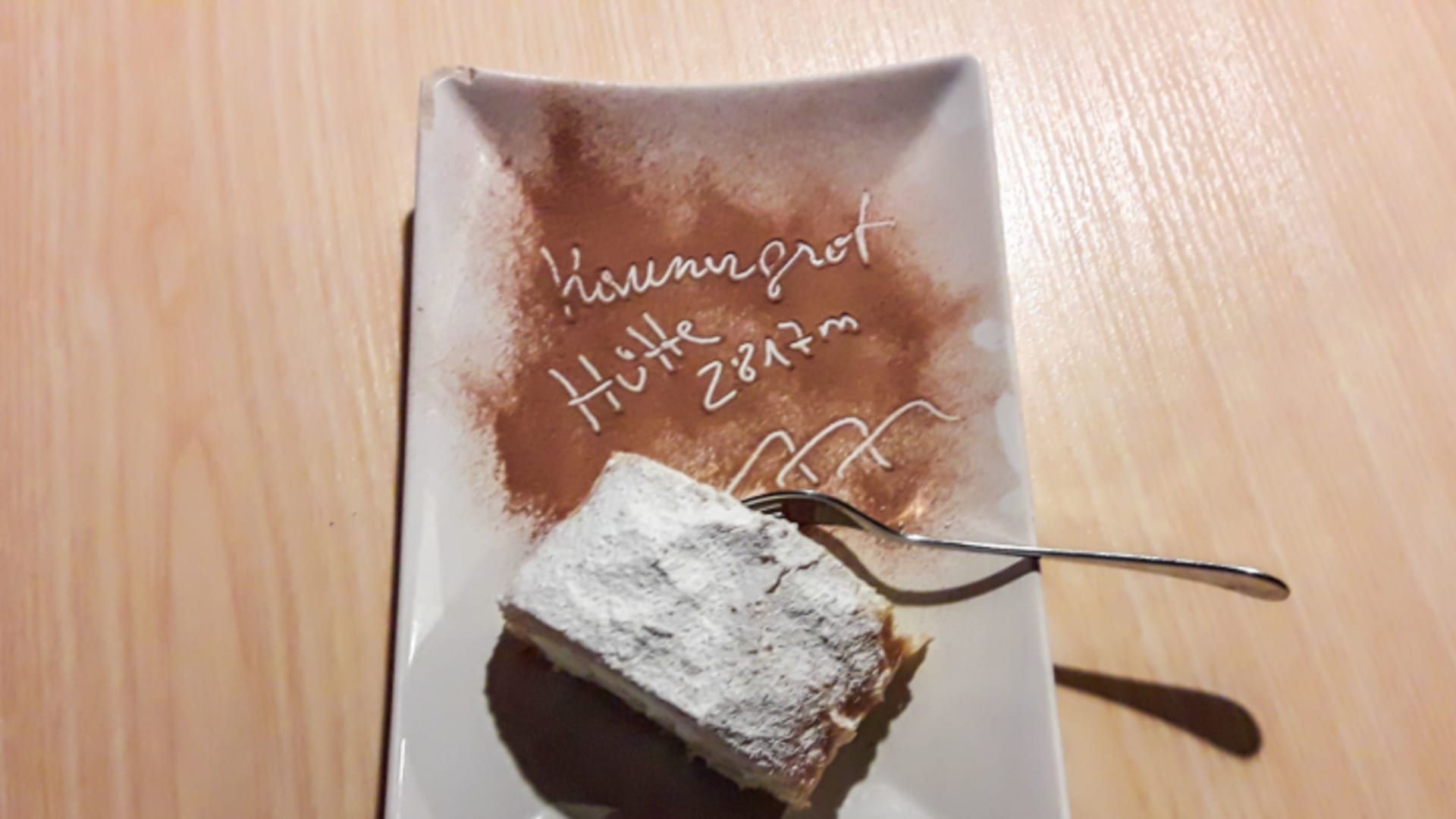 Desserteller mit handgeschriebenem Kaunergrathütte-Schriftzug und Kuchen auf Holztisch.