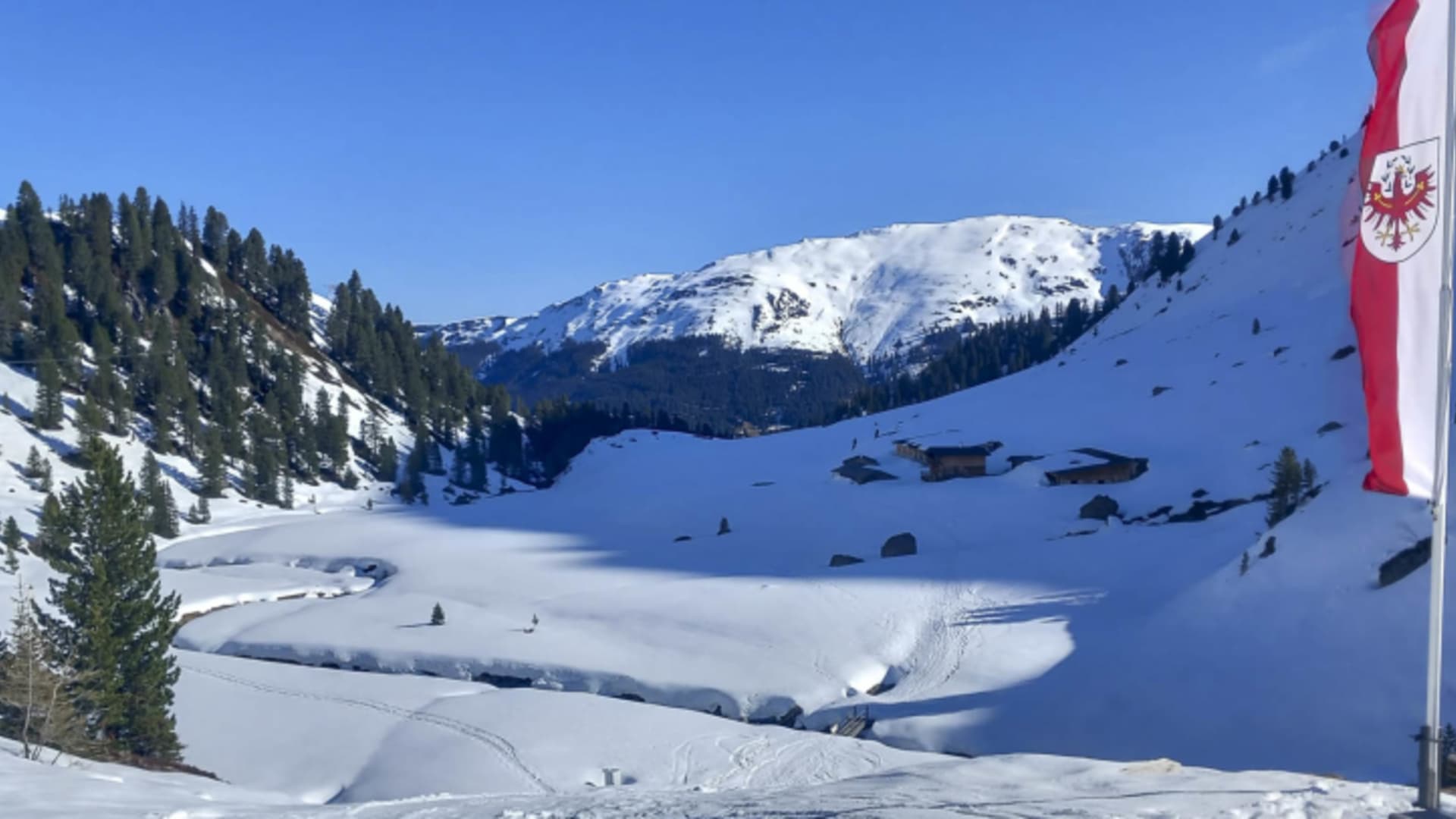 Panoramablick auf verschneites Hochtal mit österreichischer Flagge von der Neuen Bamberger Hütte.