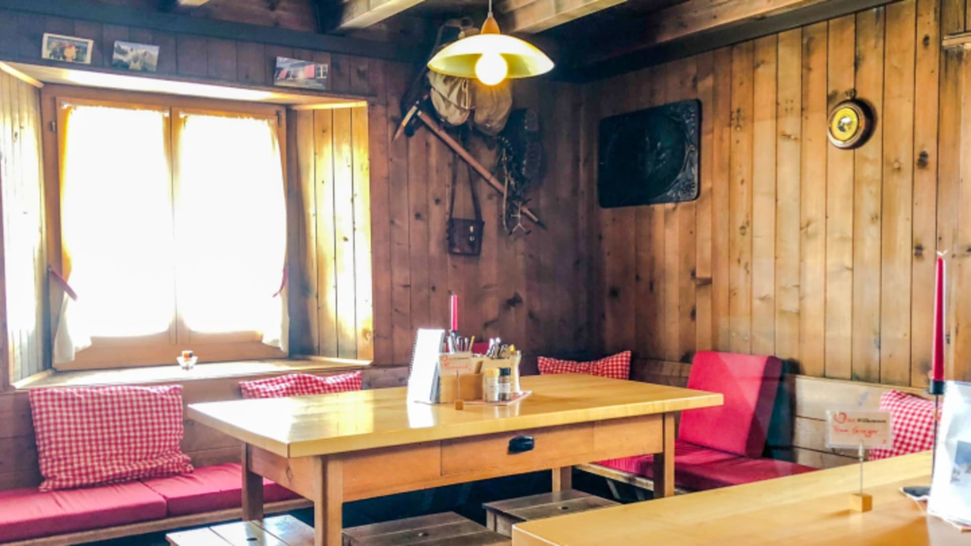 Gemütlicher Gastraum der Trifthütte mit traditioneller Holzverkleidung und rot-weiß karierten Polstern.