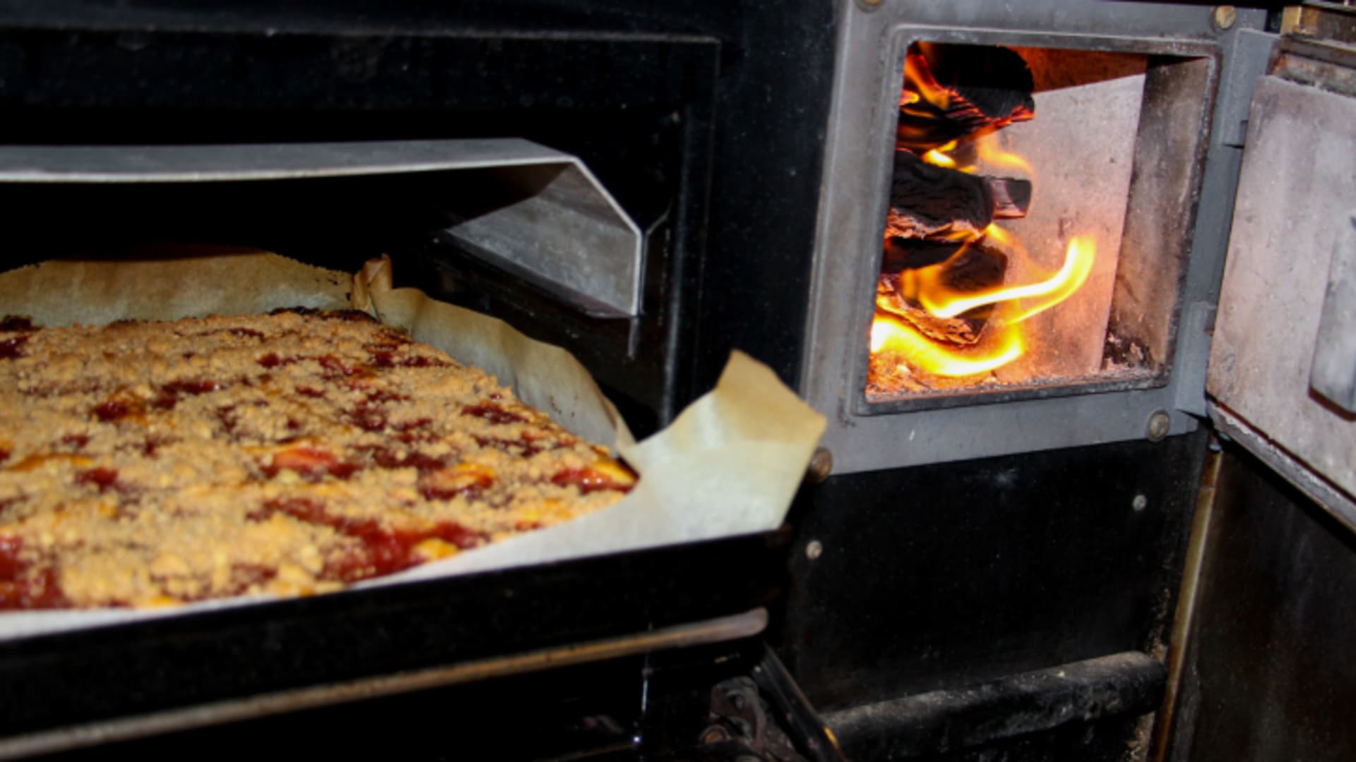 Traditioneller Holzofen mit brennendem Feuer in der Küche der Trifthütte, Pizza wird gerade gebacken.