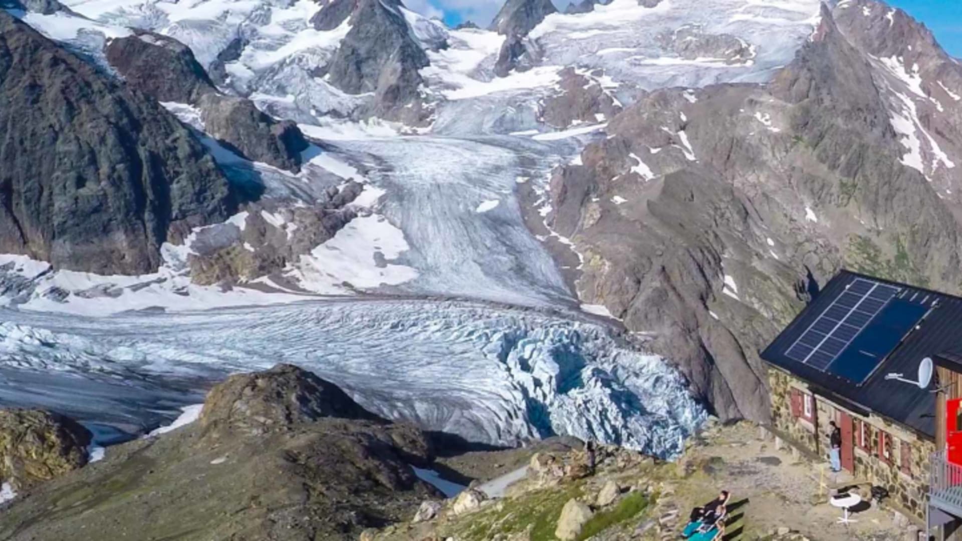 Luftaufnahme der modernen Trifthütte mit Solarpanels vor großem Gletscher in den Urner Alpen der Schweiz.