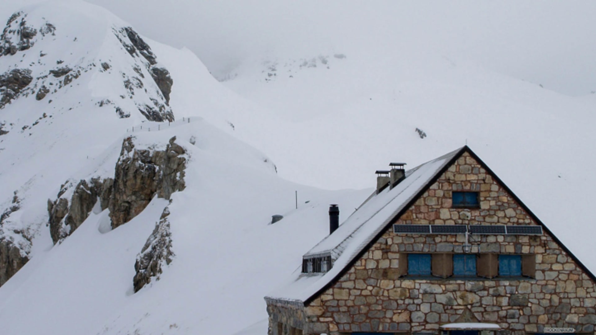 Die verschneite Pfälzerhütte steht im Winter tief eingeschneit am Felshang.