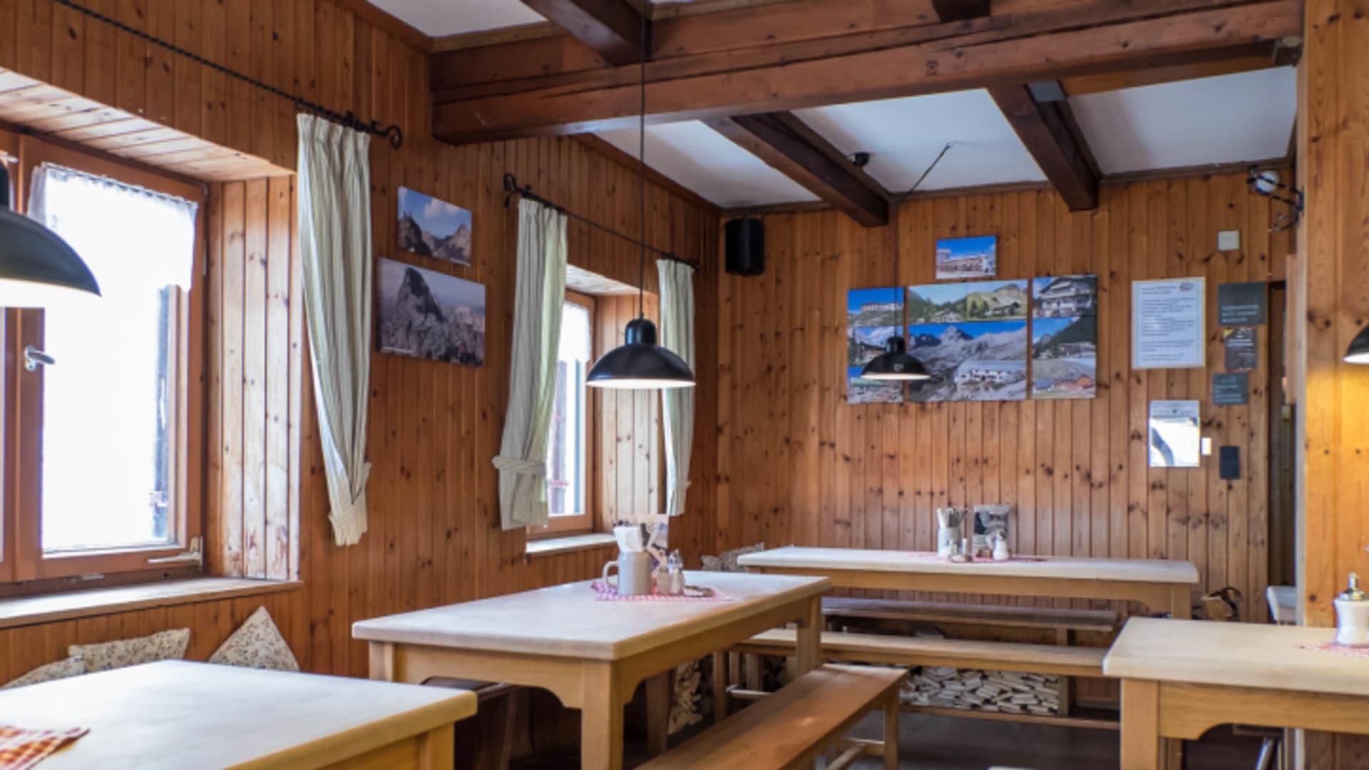 Heller Gastraum der Knorrhütte mit großen Fenstern, karierten Vorhängen und mehreren Holztischen für Gäste.