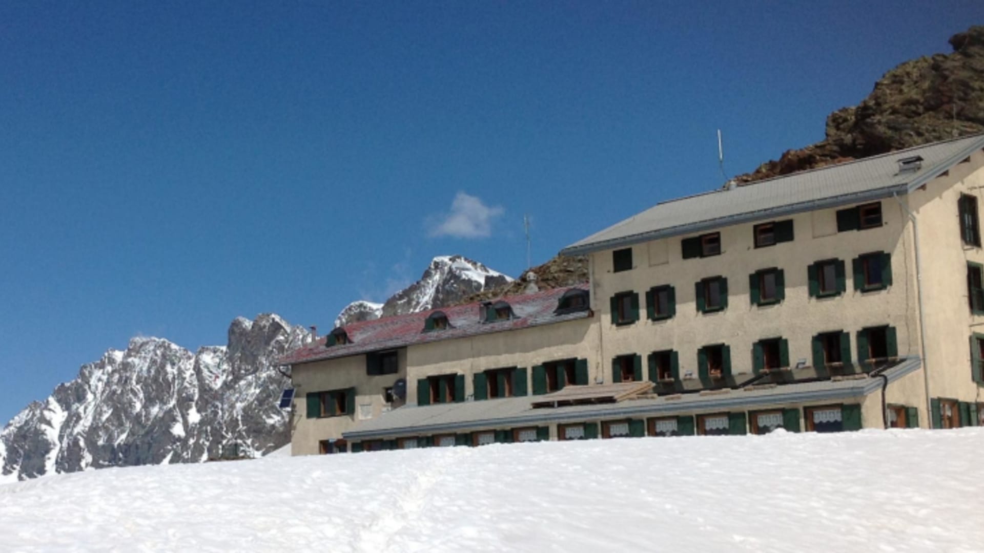 Rifugio Marinelli Bombardieri im Winterkleid mit verschneiter Hochebene und Felsgipfeln der Bernina-Alpen.