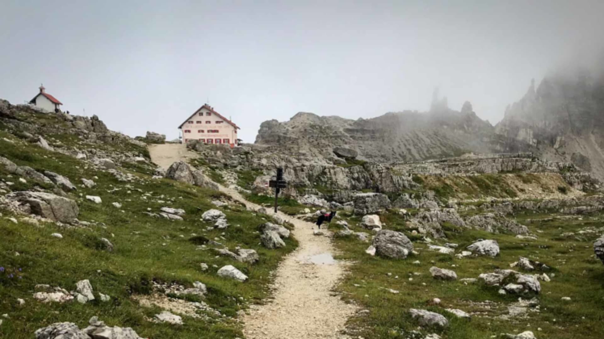 Wanderweg führt zur Drei Zinnen Hütte auf 2.405 m mit rot-weißer Markierung und Holzkreuz in den Dolomiten.