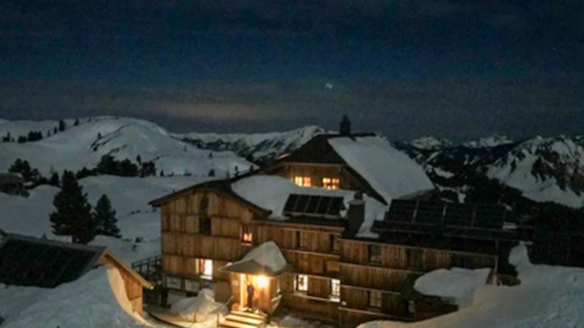 Nachtaufnahme des beleuchteten Wiesberghaus in verschneiter Winterlandschaft mit warmem Licht aus den Fenstern.