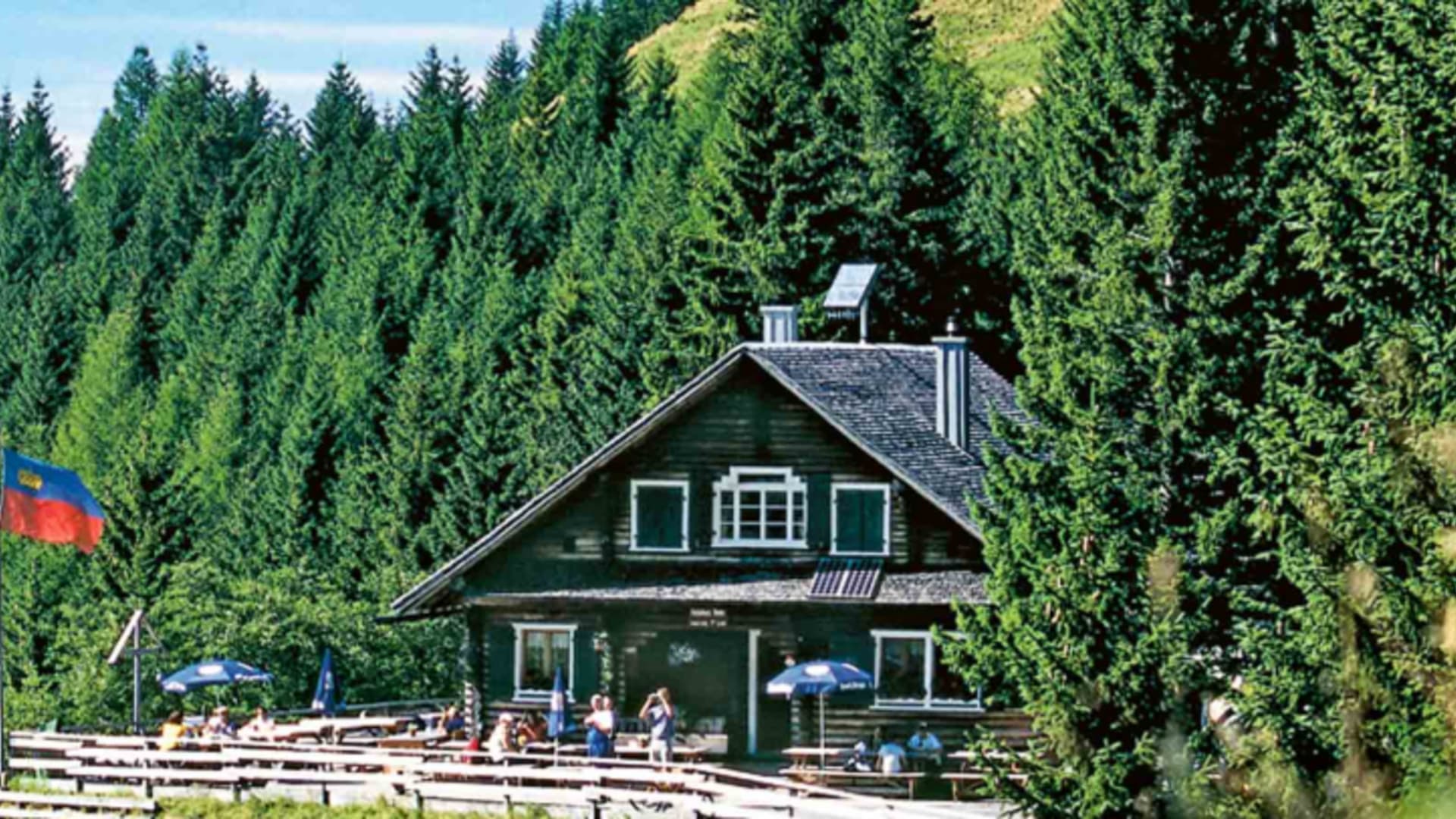 Außenansicht der Gafadurahütte mit grüner Fassade und Holzterrasse voller Gäste.