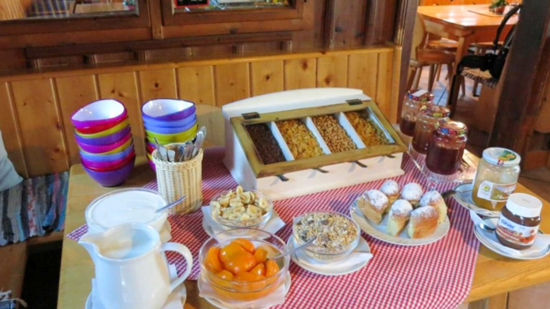 Frühstücksbuffet der Hesshütte mit Müsli, Brötchen und Marmelade auf rot-weiß kariertem Tischtuch.