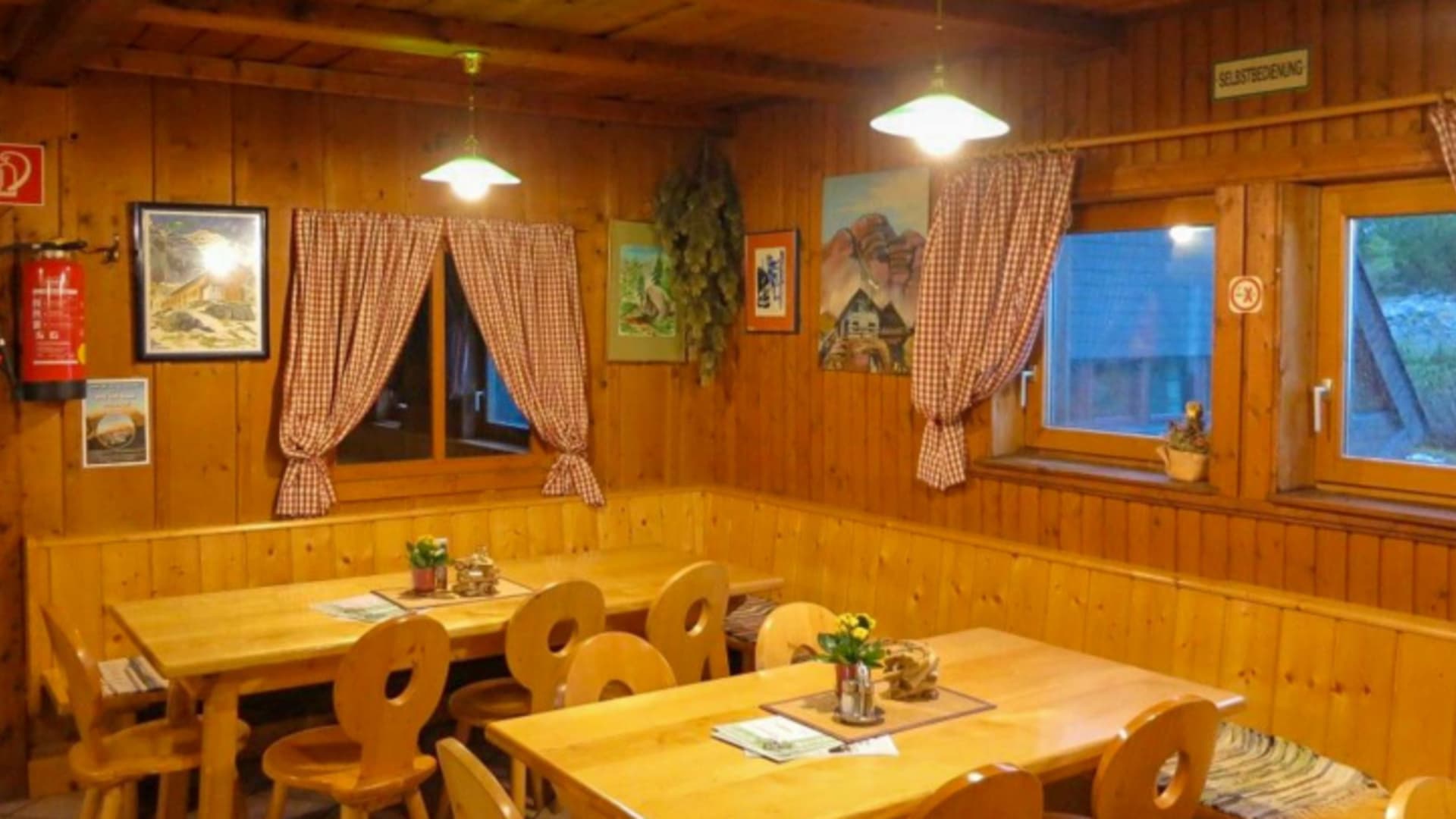 Traditionelle Gaststube der Hesshütte mit vollständig holzverkleideten Wänden und karierten Vorhängen.