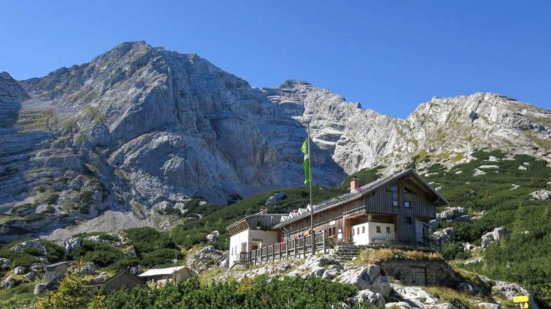 Panoramaaufnahme der Hesshütte mit grünen Fensterläden vor schroffer Felswand aus Kalkstein.