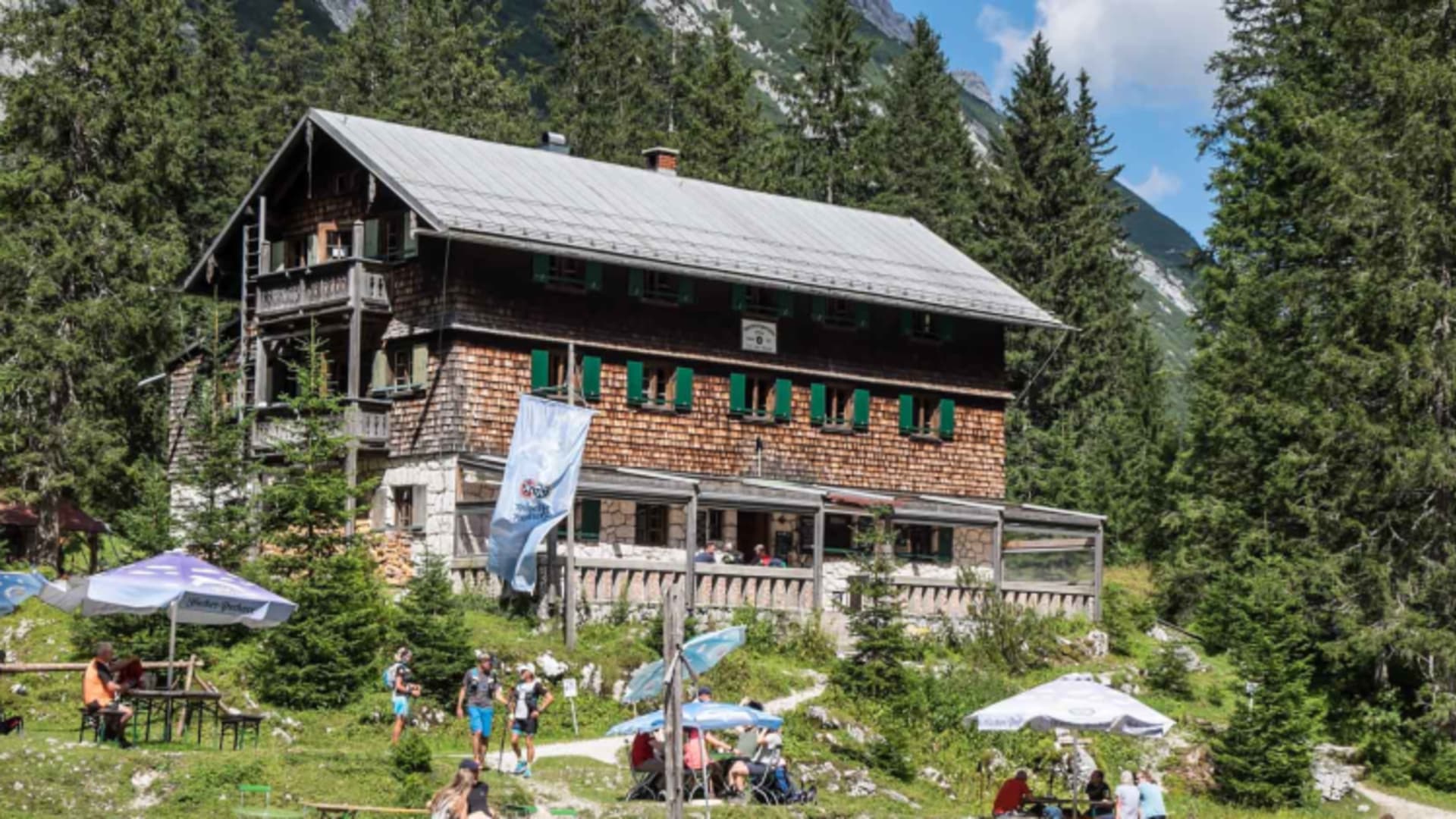 Wanderer entspannen vor der Reintalangerhütte auf der Sonnenterrasse mit Bierbänken und Sonnenschirmen.