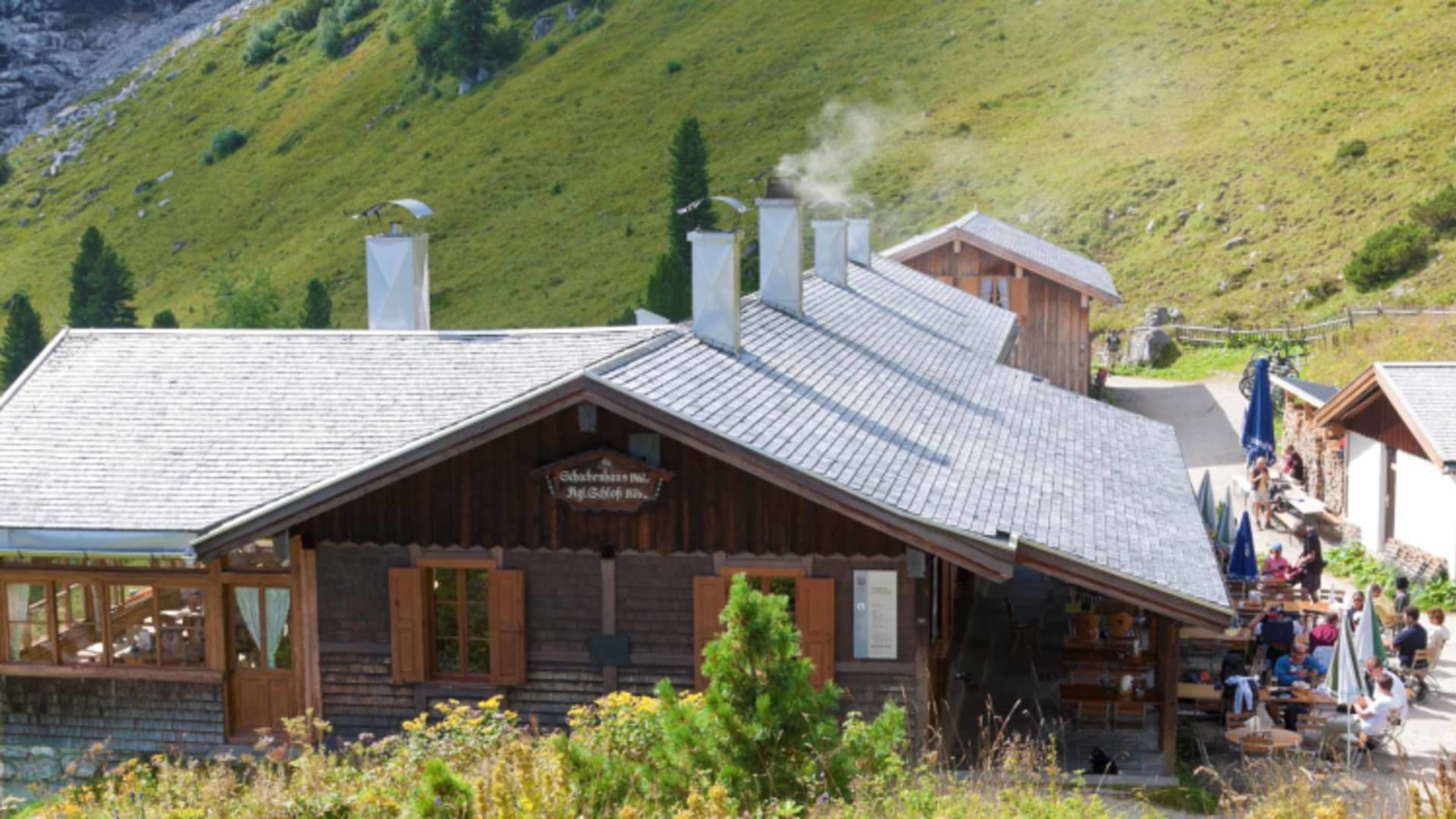 Das Schachenhaus zeigt traditionelle Alpenarchitektur mit rauchenden Kaminen und Terrasse voller Gäste.