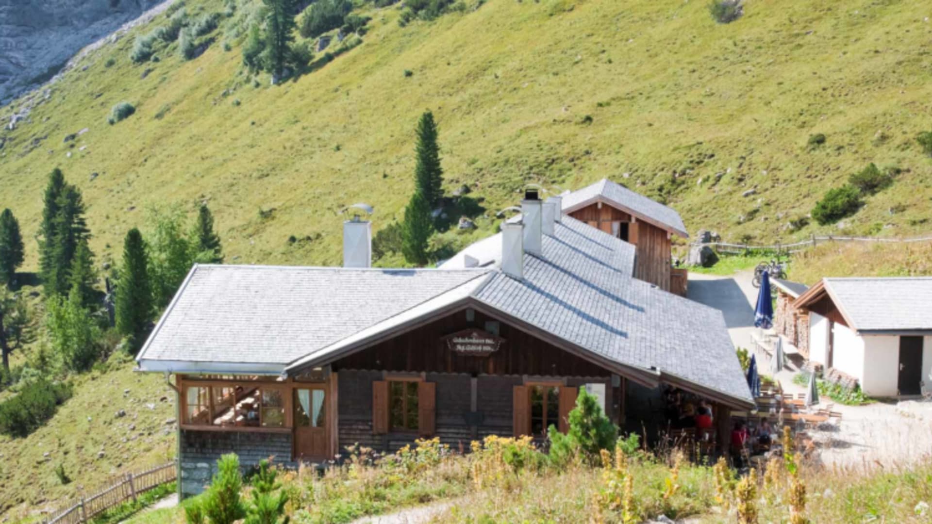 Das Schachenhaus mit Natursteinsockel und Holzfassade liegt auf grüner Almwiese.