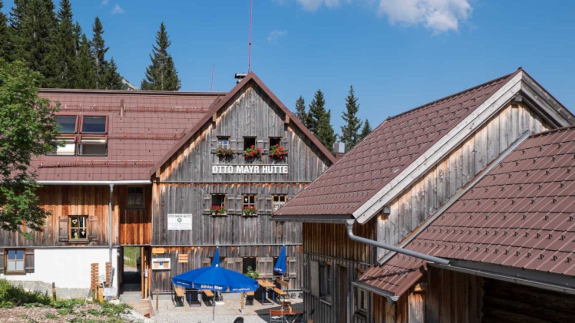 Die Otto Mayr Hütte steht inmitten dichter Nadelwälder mit traditioneller Holzfassade und modernem Anbau bei Sonnenschei
