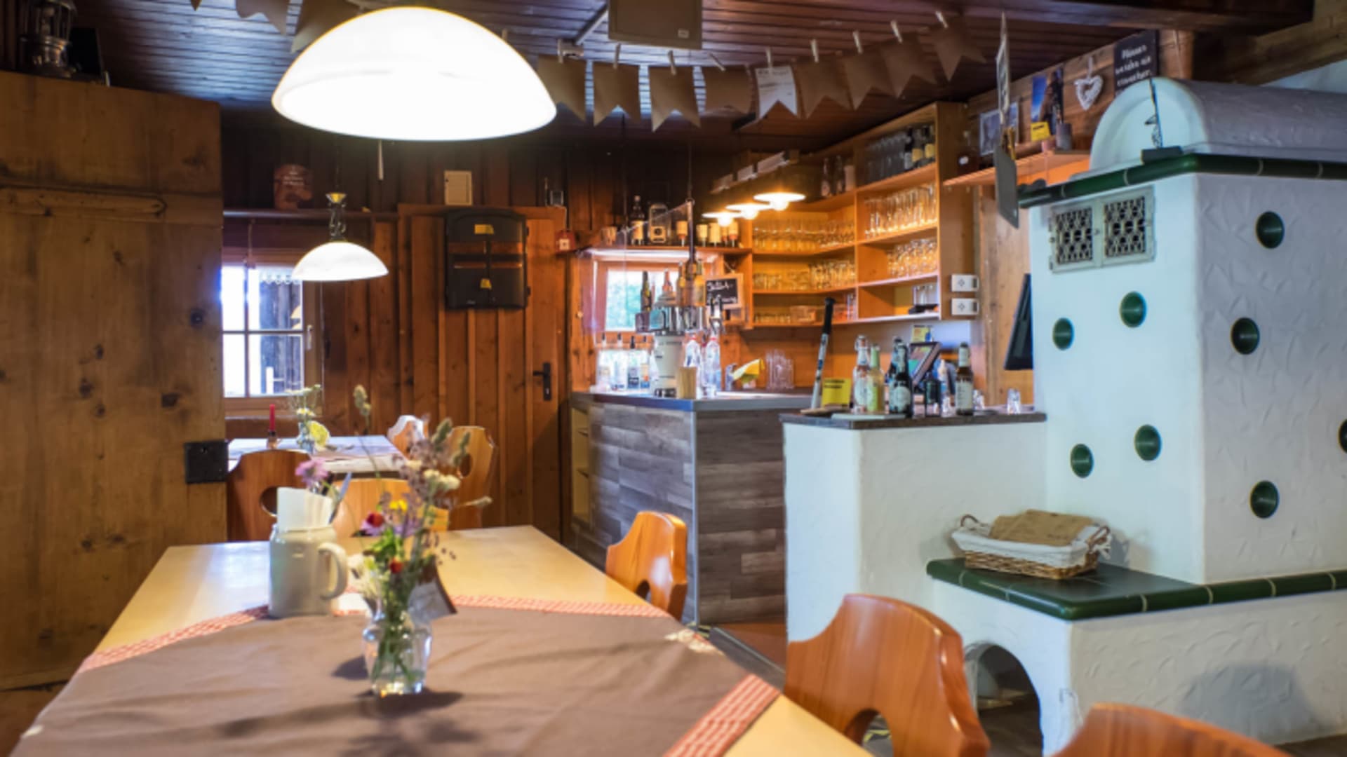 Rustikale Gaststube der Otto Mayr Hütte mit weißem Kachelofen und traditioneller Holzeinrichtung im Alpenvereinsstil.
