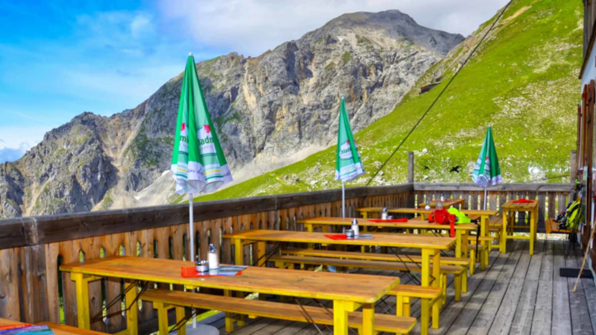 Sonnenterrasse des Guttenberghaus mit gelben Holztischen und grünen Sonnenschirmen.