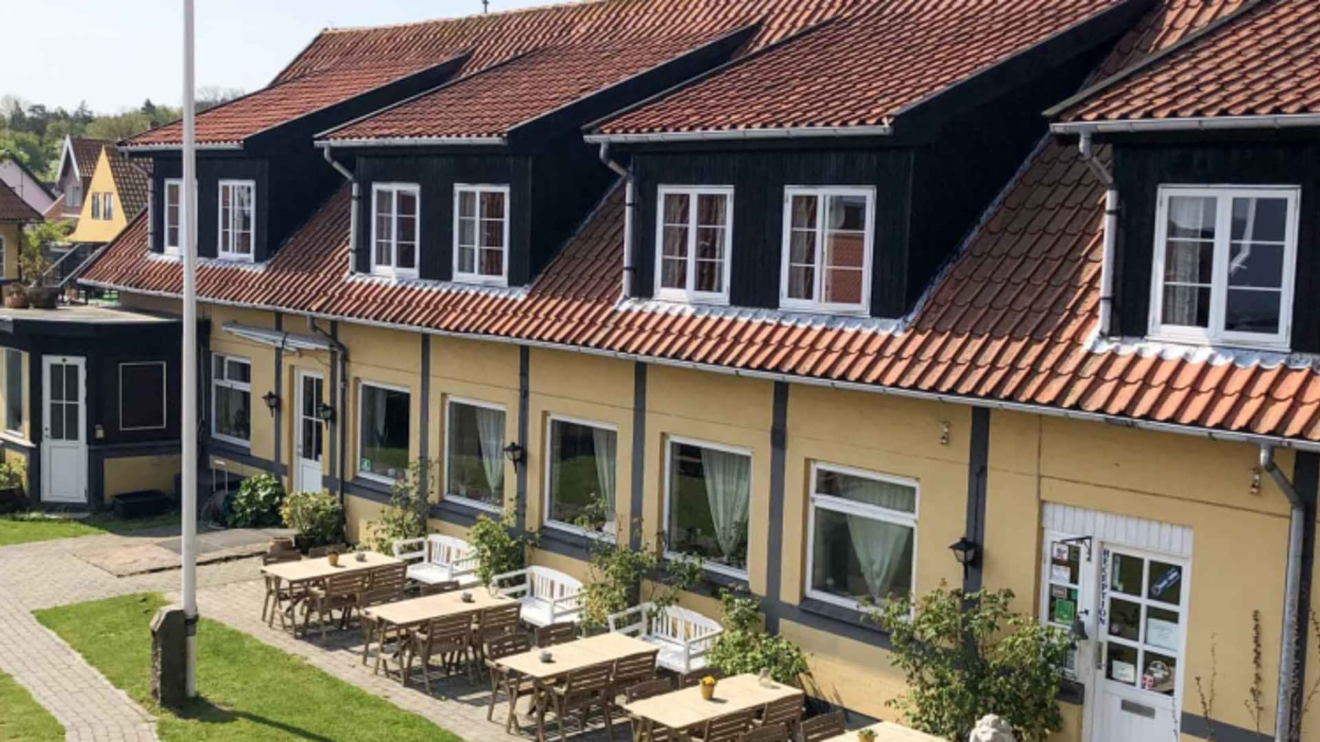 Außenansicht der Pension Slaegtsgaarden mit gelber Fassade und Holztischen auf der Terrasse.