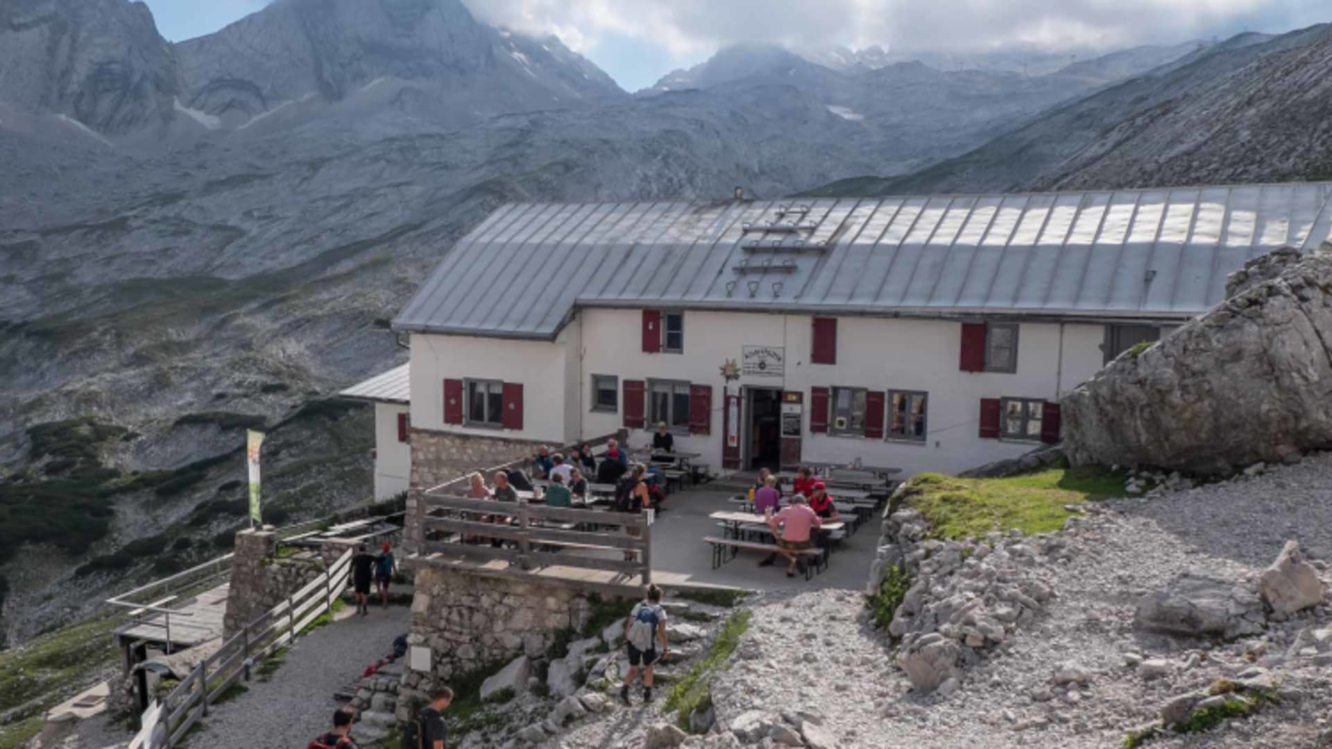 Panoramaaufnahme der Knorrhütte mit Bergwanderern auf der Terrasse in hochalpiner Umgebung.