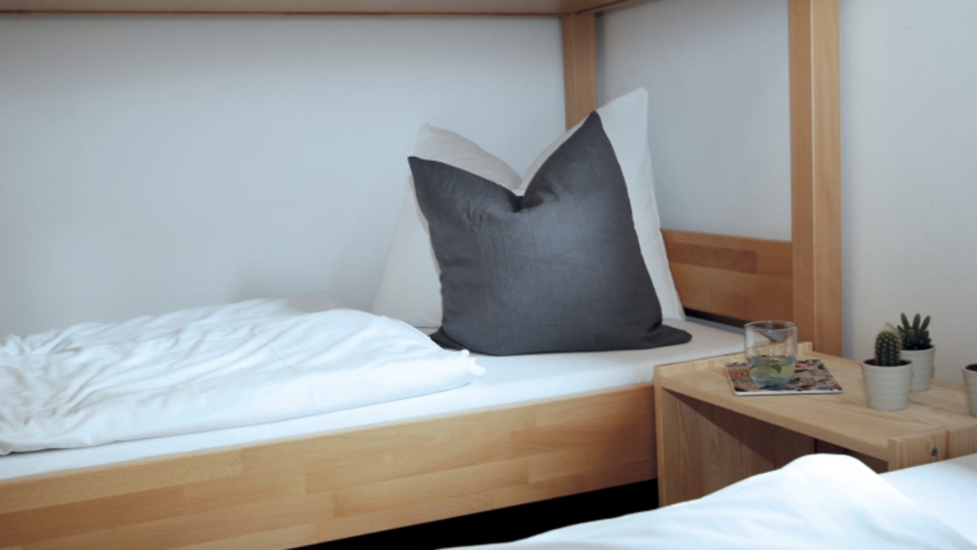 Zweibettzimmer im Berg Blick Hostel mit hellem Holzmobiliar, weißer Bettwäsche und modernem Nachttisch zwischen den Betten.