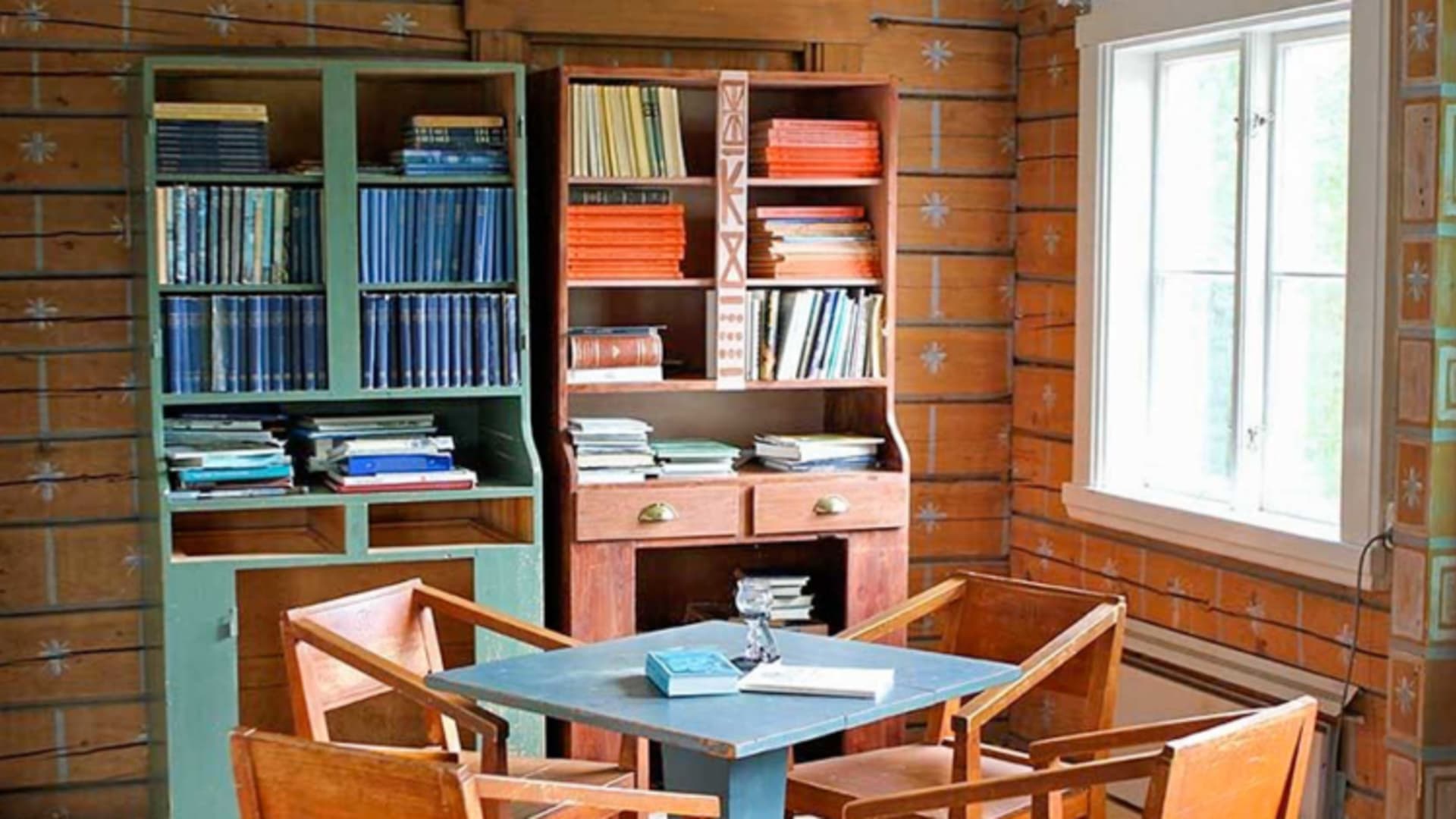 Der Aufenthaltsraum der STF Kvikkjokk Fjällstation zeigt rustikale Holzausstattung mit blauem Tisch und Bücherregalen.
