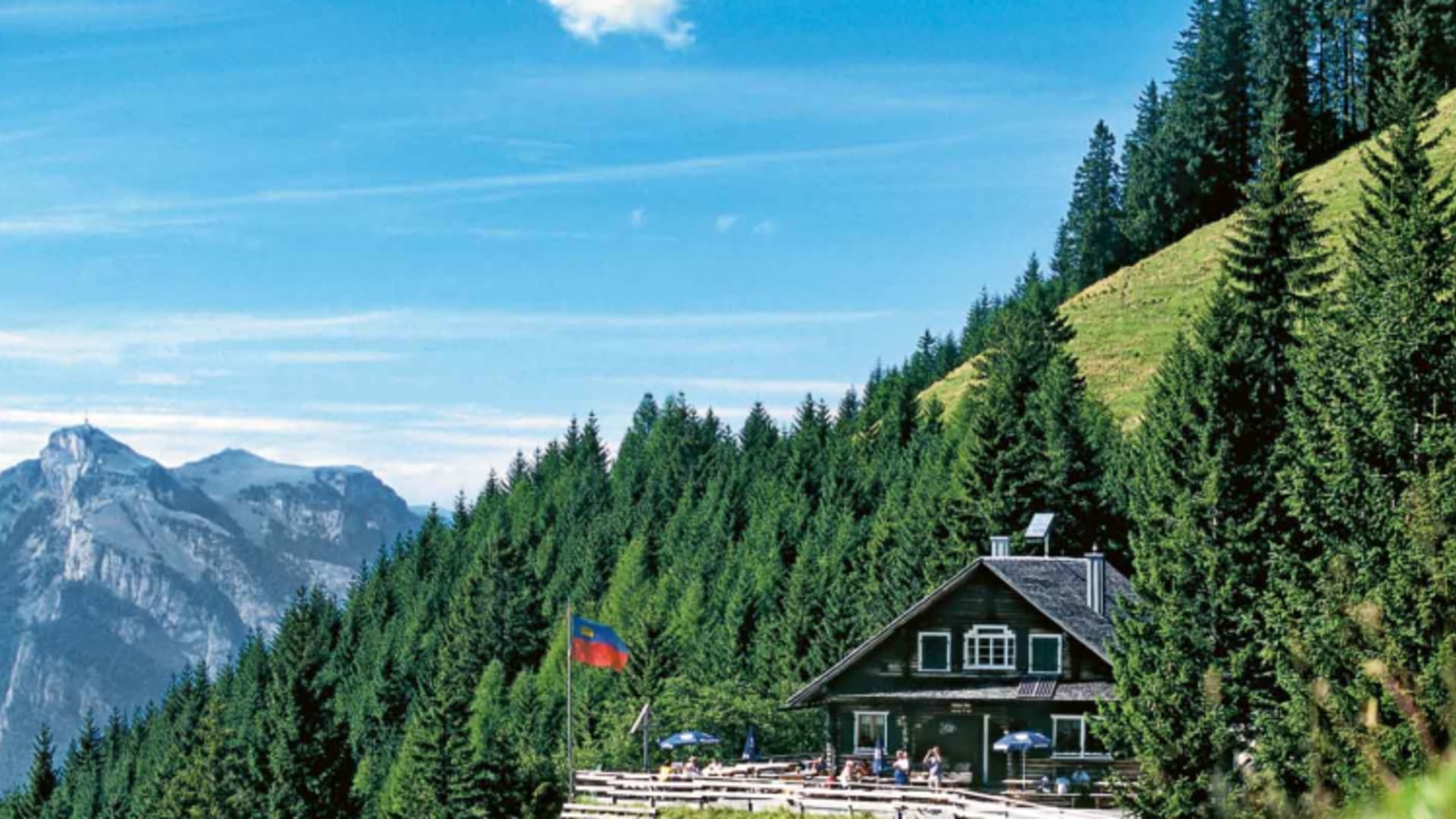 Die Gafadurahütte steht auf grüner Almwiese mit Terrasse und Blick auf die Rätikon-Bergkette.