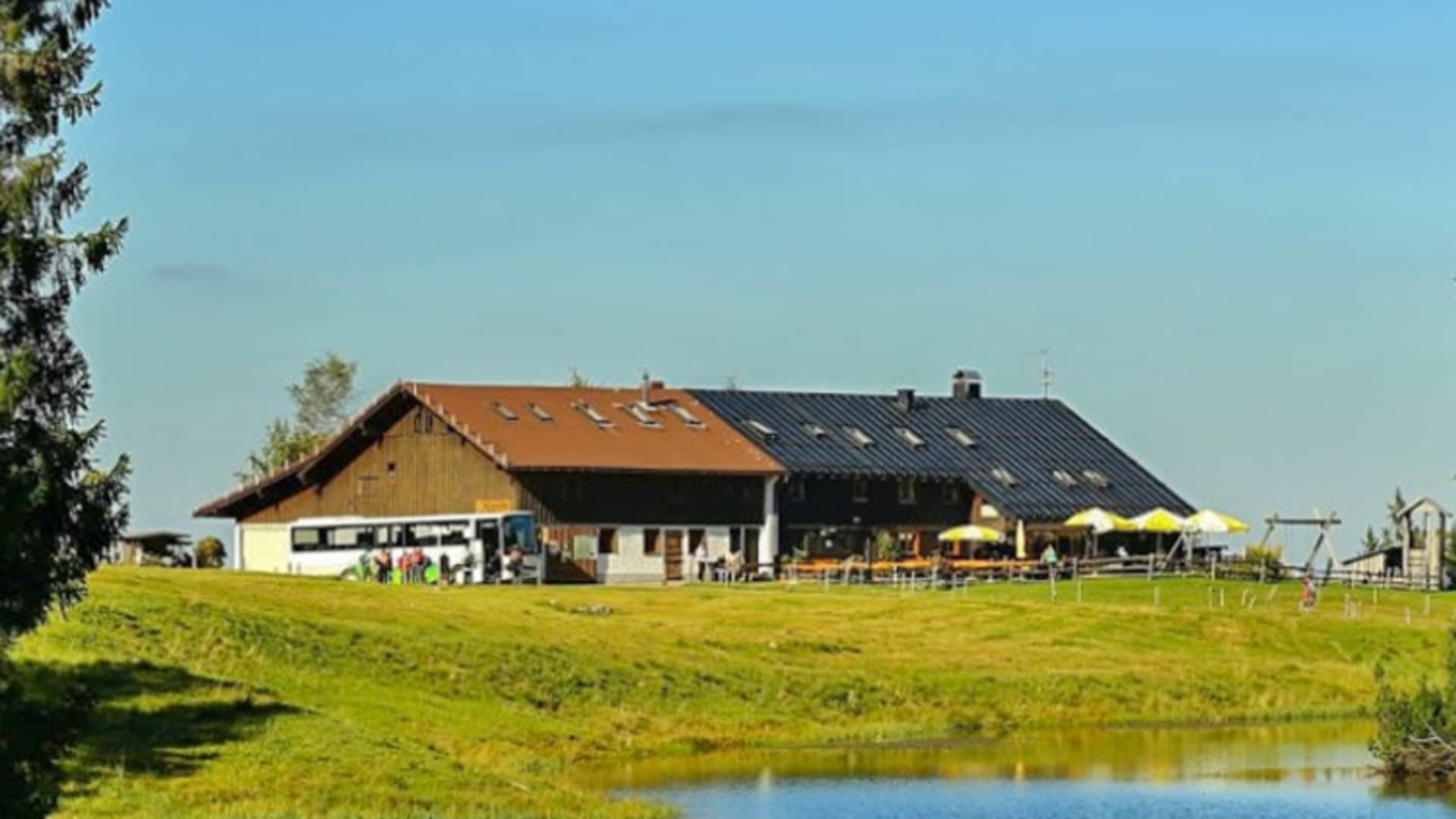 Der Alpengasthof Hörmoos zeigt alpine Architektur mit Terrasse, gelben Sonnenschirmen und Teich im Vordergrund.