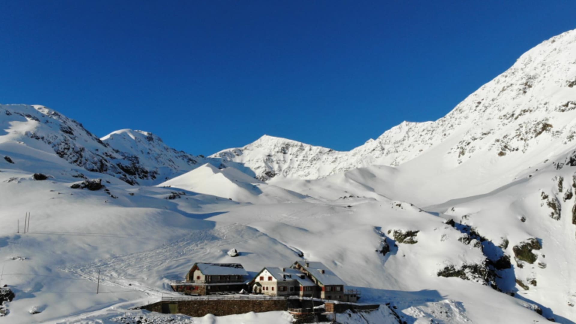 Winterpanorama des Rifugio Branca im verschneiten Hochtal mit umgebenden Bergen und Seilbahninfrastruktur im Ortlergebiet.