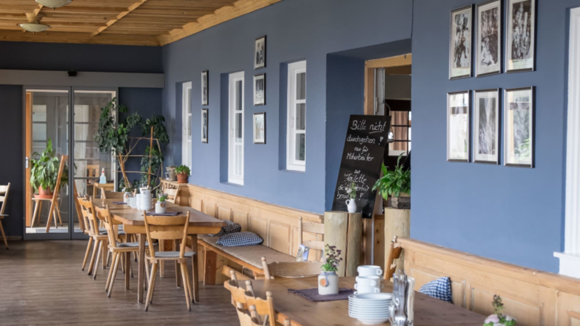 Gaststube im Kreuzeckhaus mit blauen Wänden, Holztischen und schwarz-weiß Fotografien an den Wänden.