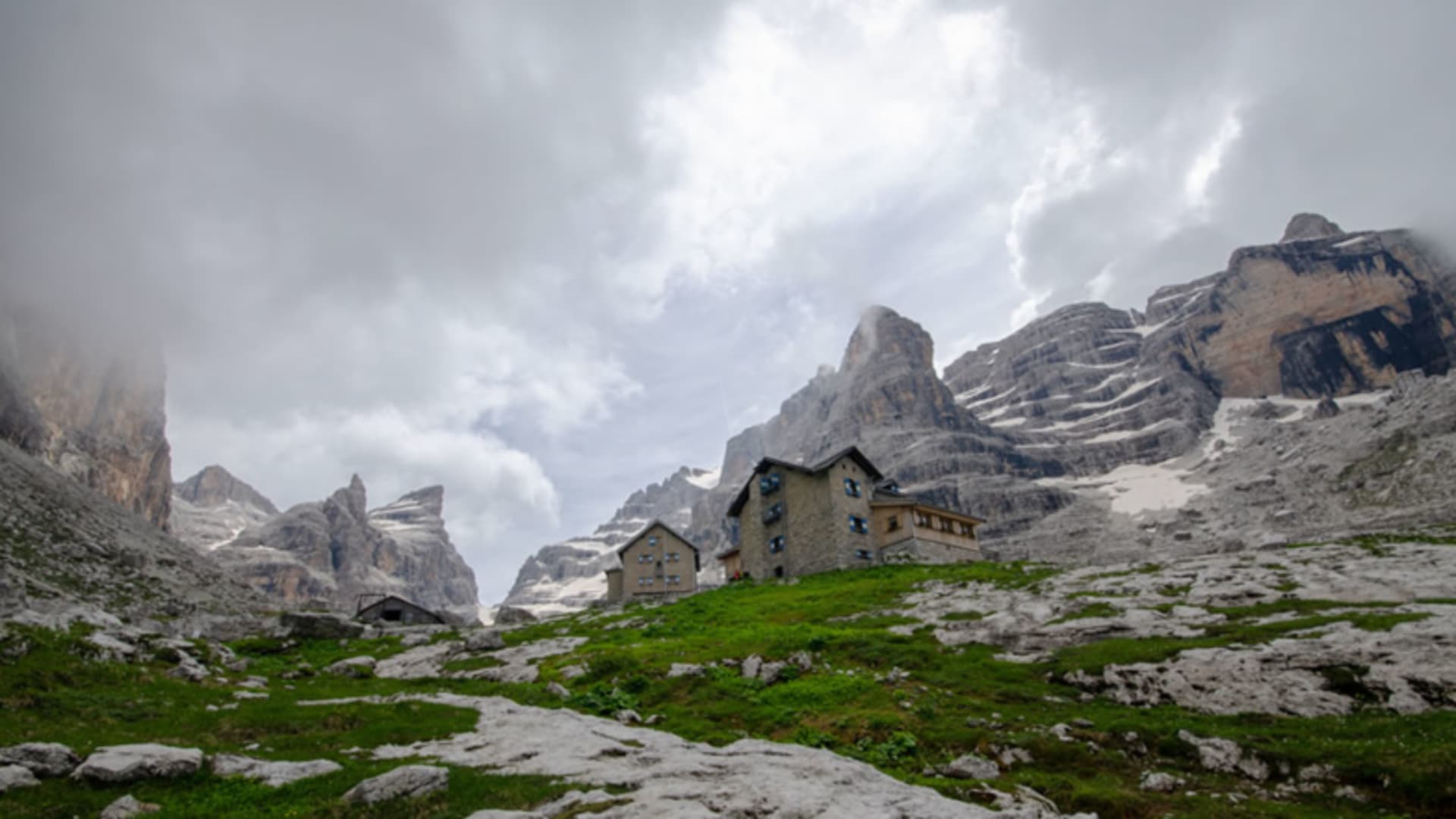 Panoramablick auf das Rifugio Tuckett mit zwei Steingebäuden vor geschichteten Kalksteinwänden der Dolomiten.